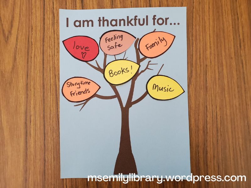 Thankful tree craft - a dark brown bare tree figure on light blue paper with a heading, "I am thankful for..." and fall colored leaves listing gratitudes: books, love, storytime friends, feeling safe, family, and music.