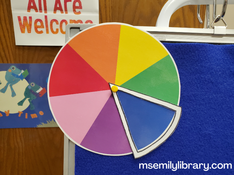 A round color wheel showing the colors red, orange, yellow, green, blue, purple, and pink, with a highlighted white outline wedge around blue, which can spin on a push pin in the middle.