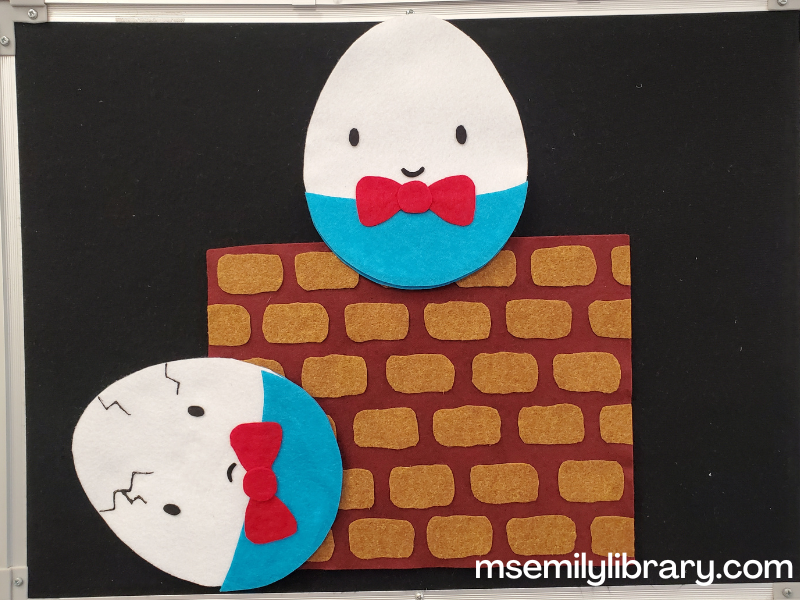 flannel of rock on the wall, with a piece of dark red felt with brown bricks. Two eggs are superimposed, one sitting at the top of the wall with a smile and a big red bowtie, the second on its side at the bottom of the wall frowning, with cracks and tie askew.