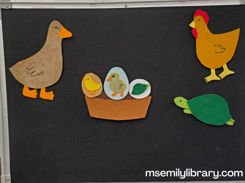flannel for three eggs in a basket, showing a simple brown basket with three eggs - a brown one with a yellow chick showing on top, a larger blue egg with a duckling, and a round white egg with a turtle. ARound the basket are a large brown/gray duck, brown hen, and green turtle.