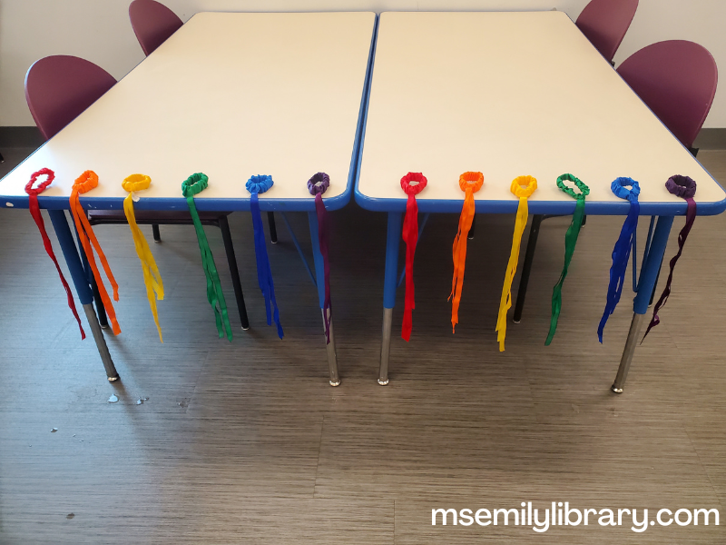 rainbow colored wrist ribbons drying on a table. The wristbands sit on the table while the ribbons drape over.